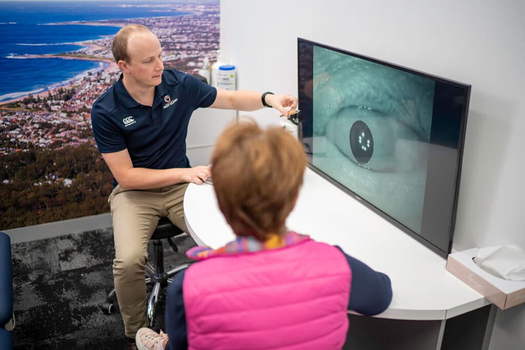 A Dizzy Clinics physiotherapist guiding a patient's gaze during a vestibular assessment, her eye movement shown magnified on a wall-mounted screen